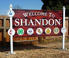 Welcome sign for Shandon with white posts, colorful emblems, and a red background
