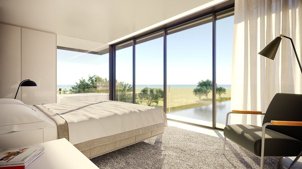 Um quarto com cama, cadeira, luminária e grandes janelas.