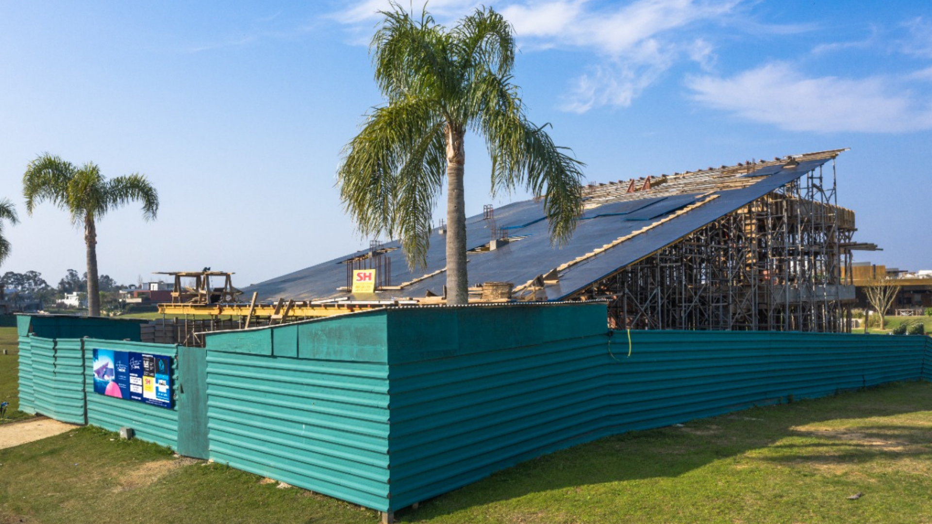 Um prédio em construção com uma cerca ao redor e palmeiras ao fundo.