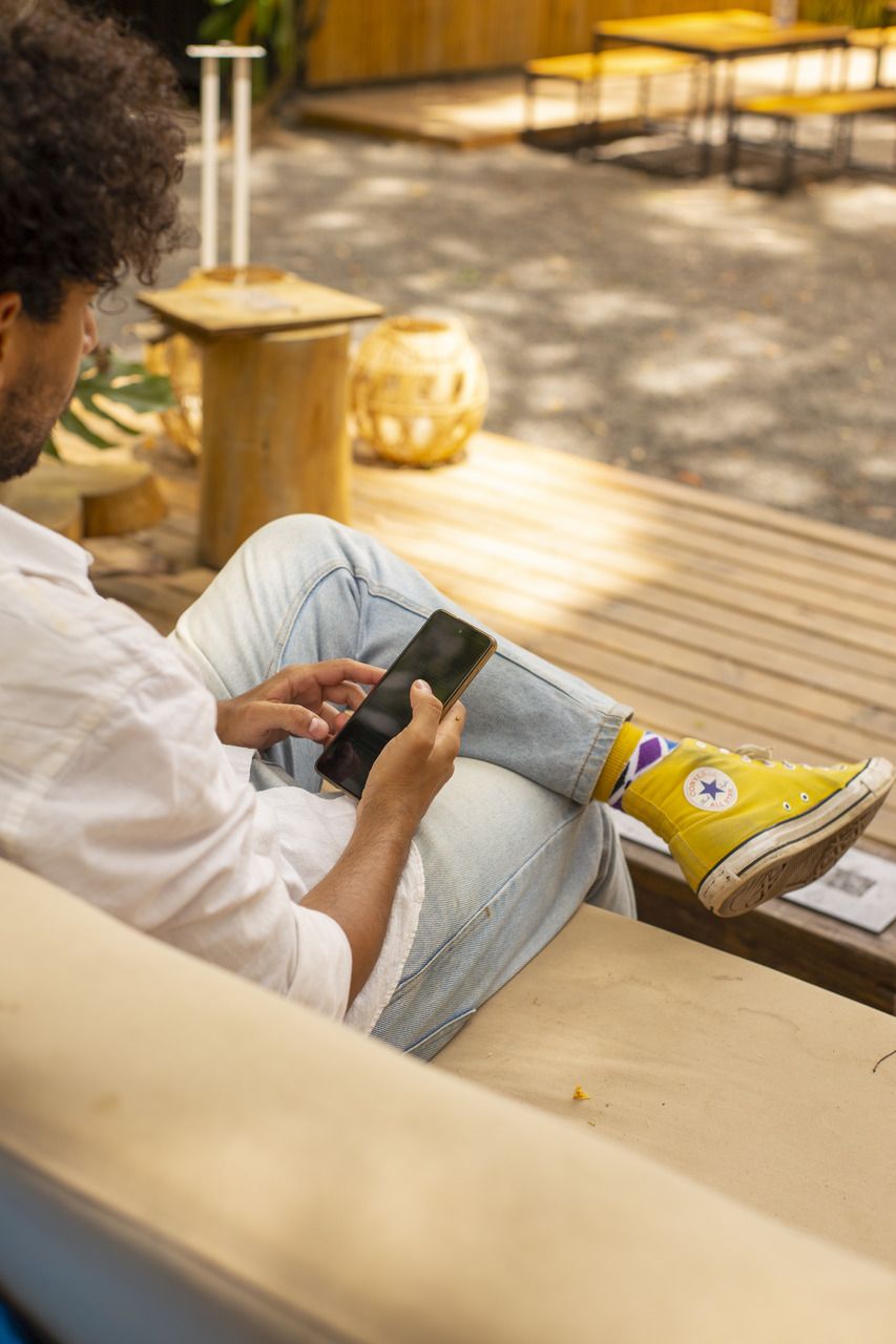 Um homem está sentado em um sofá usando um telefone celular.