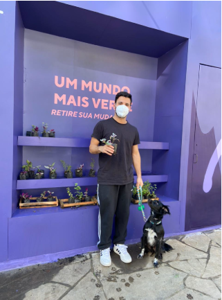 Um homem usando máscara fica ao lado de um cachorro em frente a uma parede que diz um mundo mais ver