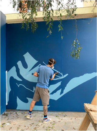 Um homem está pintando um mural em uma parede azul.