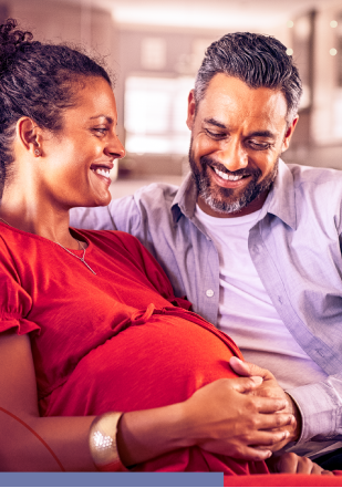 Um homem e uma mulher grávida estão sentados em um sofá e sorrindo um para o outro.
