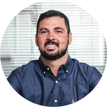 Um homem com barba está vestindo uma camisa azul e sorrindo.