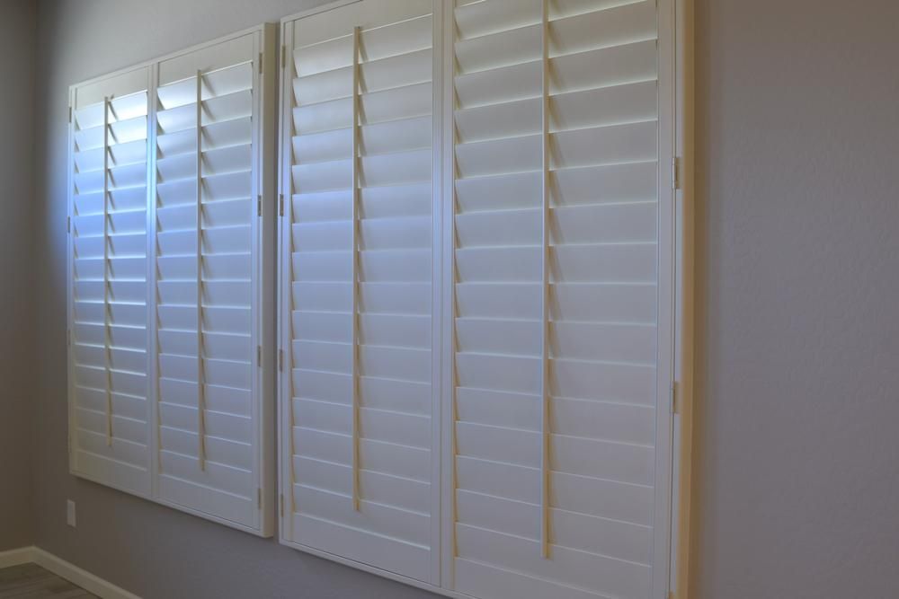A White Shutters Are Hanging On A Wall In A Room — Outdoor Blinds In Bateau Bay, NSW