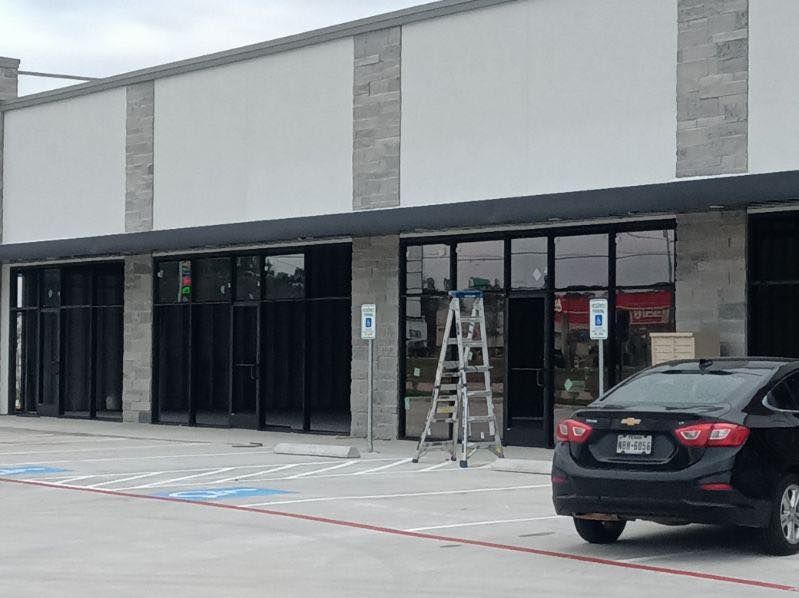 Exterior of a commercial building with black-framed windows, awnings, and a car parked in front.