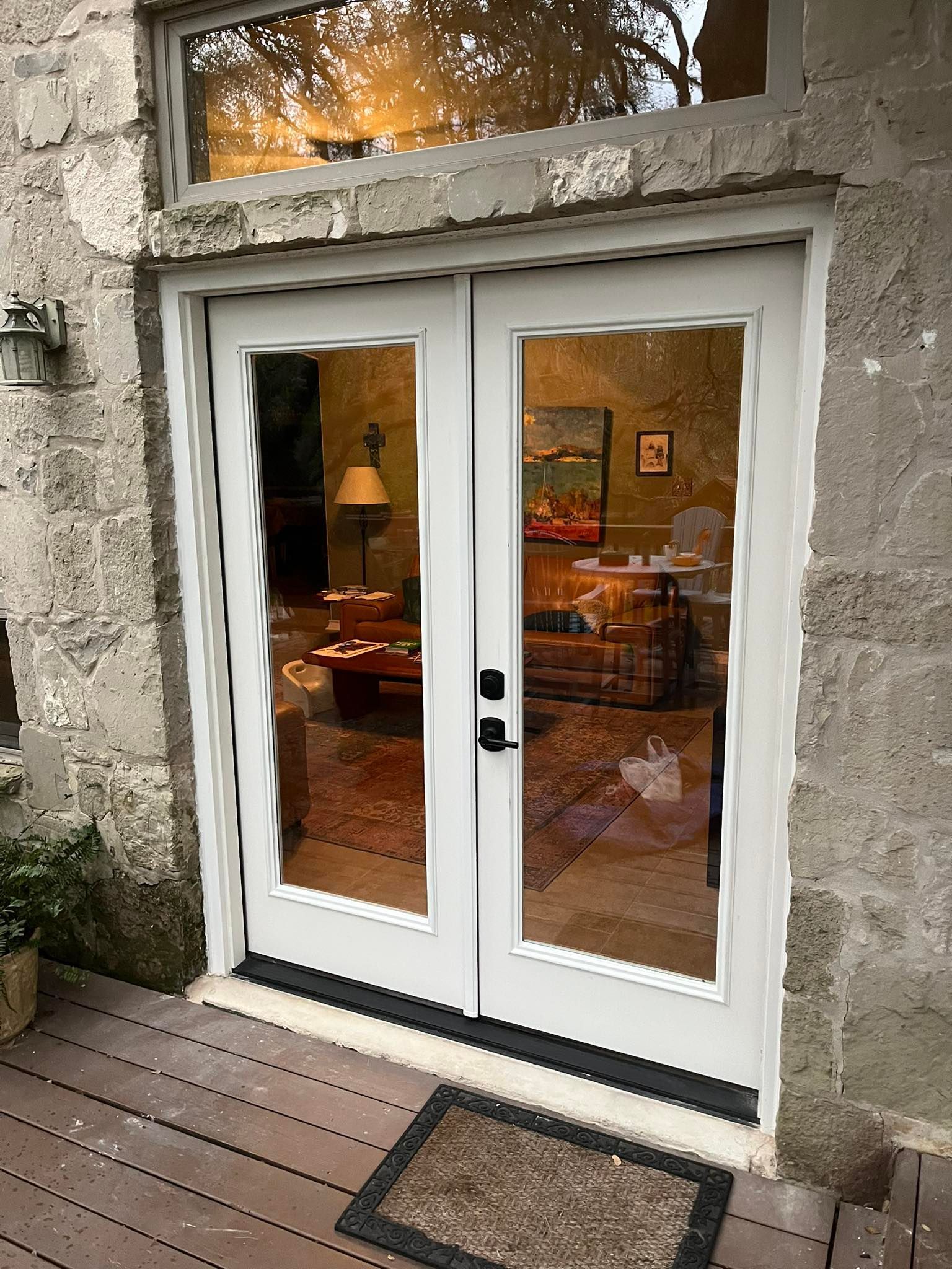 White French doors with glass panes, reflecting an interior with furniture, in a stone building.