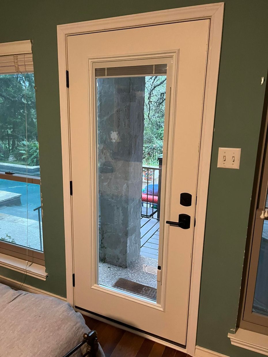 White door with glass panel, leading to a patio. Green wall, dark door handle, and a light switch visible.