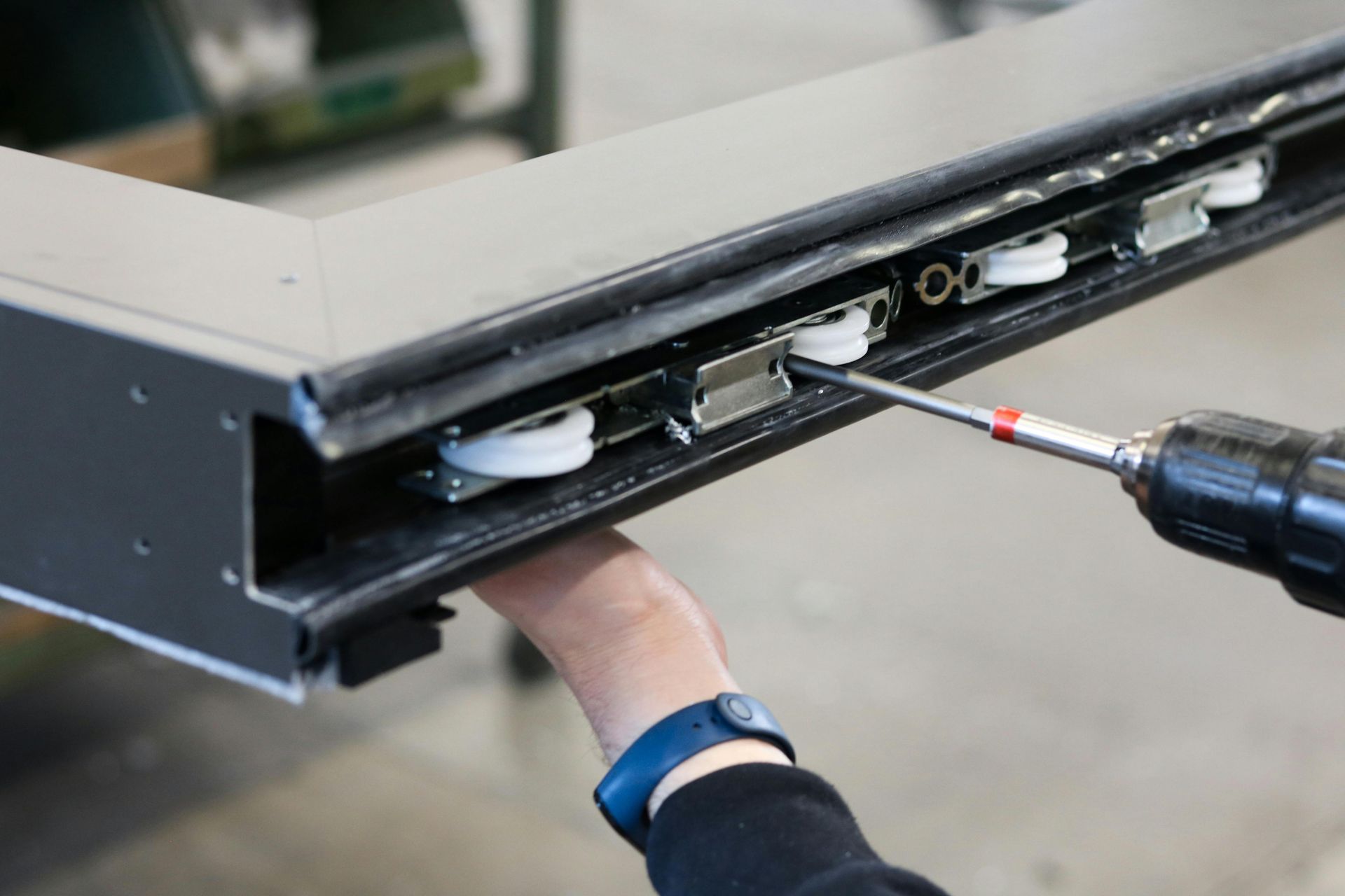 Person using a screwdriver to repair the underside of a gray desk or cabinet.