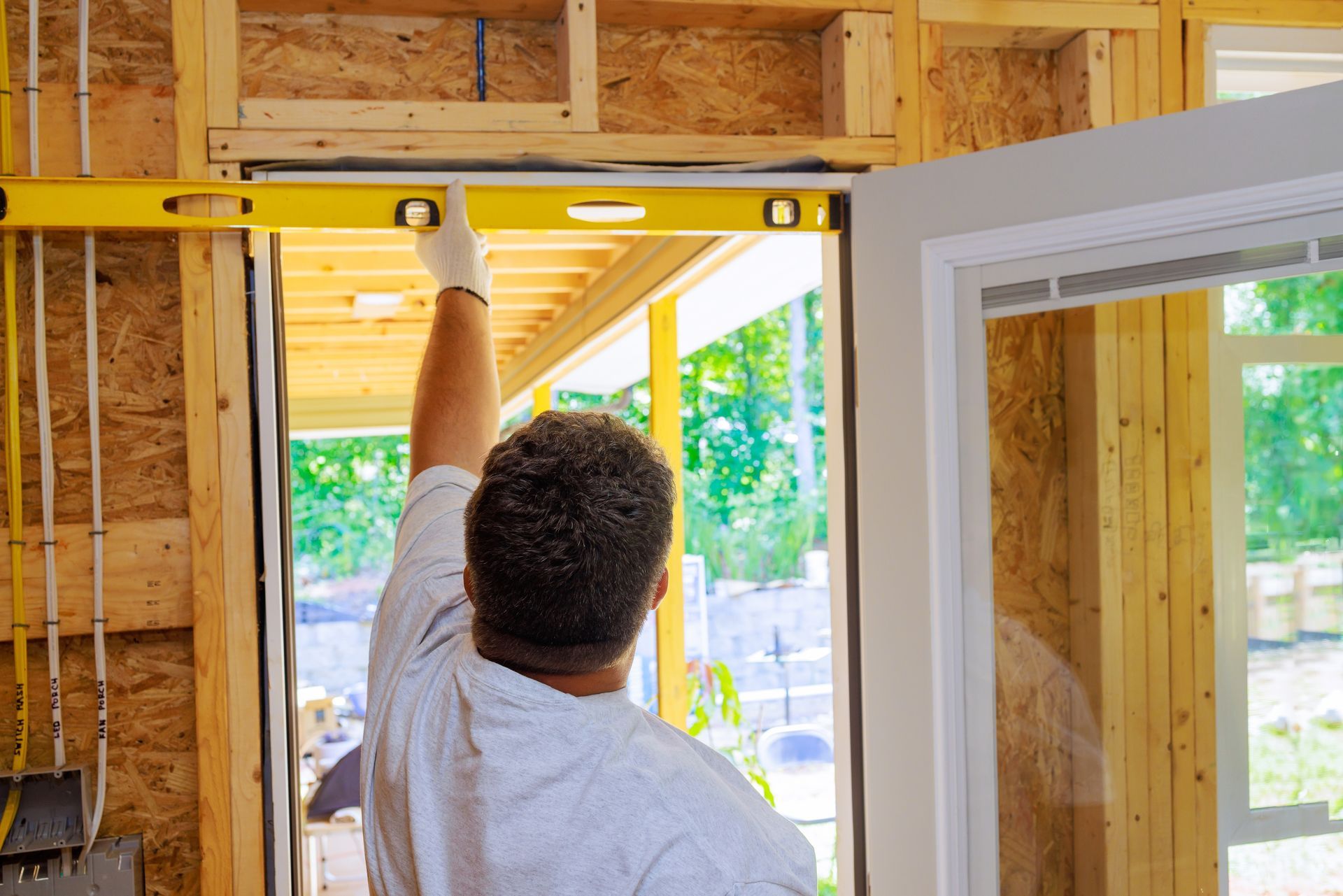 A construction worker uses a yellow spirit level to check the header of a door frame in a wooden stud wall.