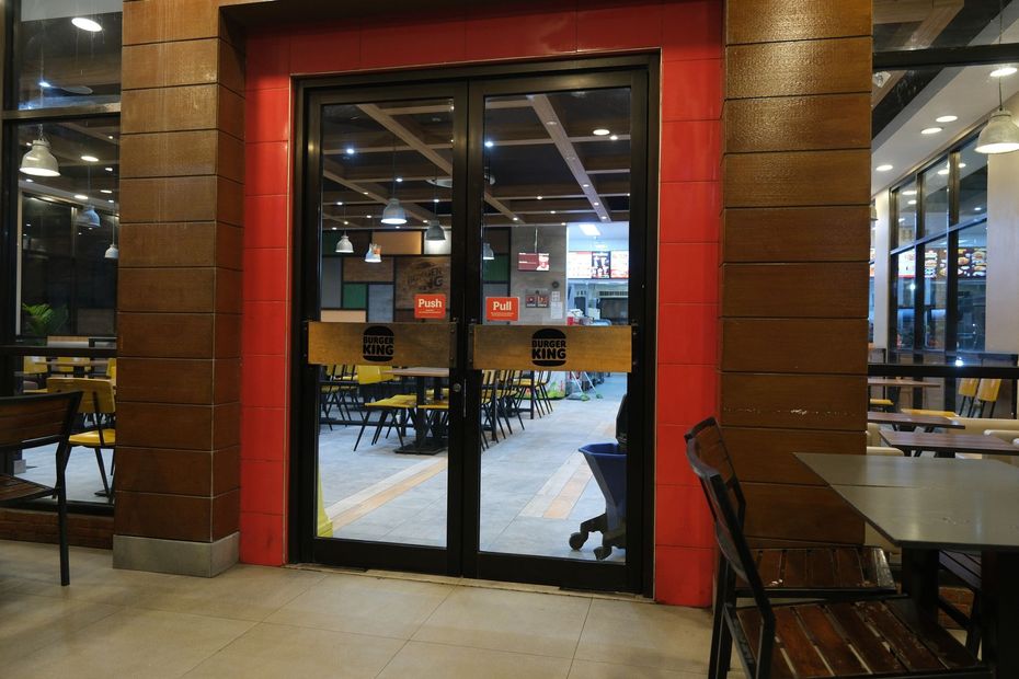 Double glass doors with black frames leading into a restaurant. Red trim, wooden paneling. Tables and chairs visible inside.