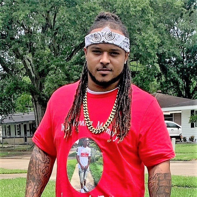 A man wearing a red shirt and a bandana is standing in front of a house.