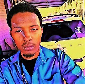 A man in a blue shirt is taking a selfie in front of a yellow car