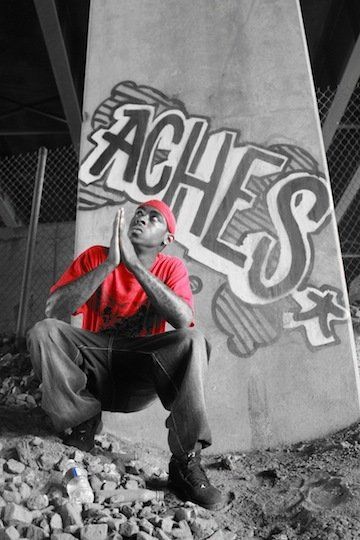 A man kneeling in front of a wall that says aches