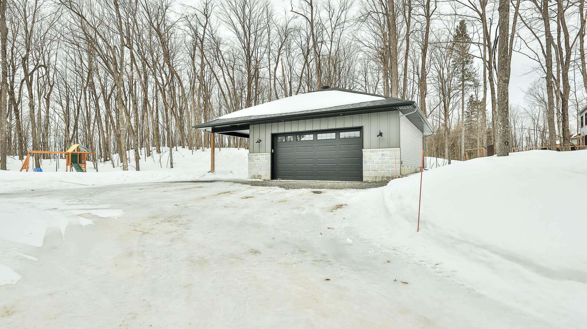 A garage is covered in snow in the middle of a snowy forest.