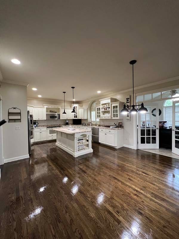 Bright, open kitchen with white cabinets, island, pendant lights, and glossy hardwood floors