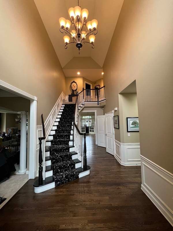 Elegant foyer with a staircase, dark wood floors, and a chandelier-lit high ceiling