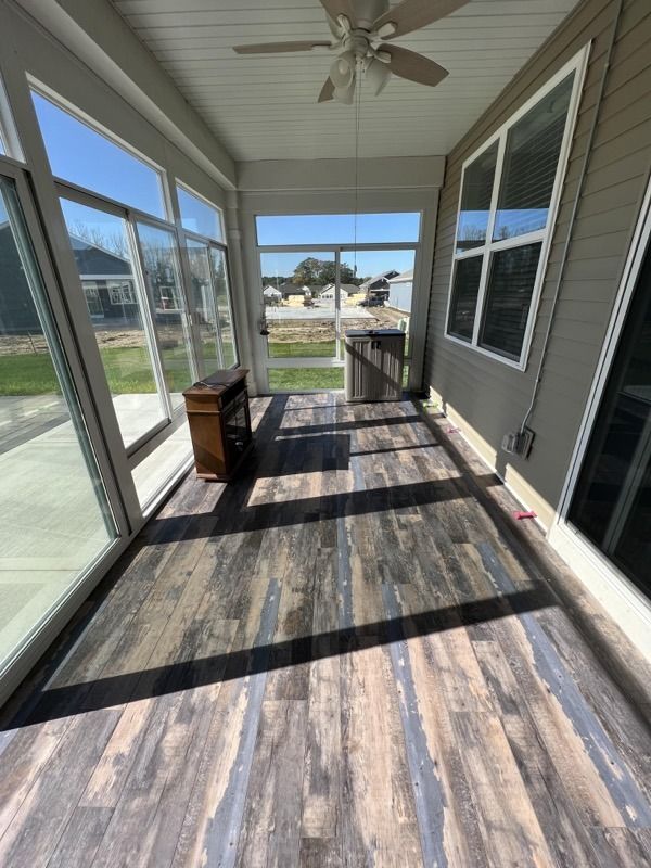 Sunlit screened porch with gray wood-look floor, ceiling fan, and view of a quiet neighborhood