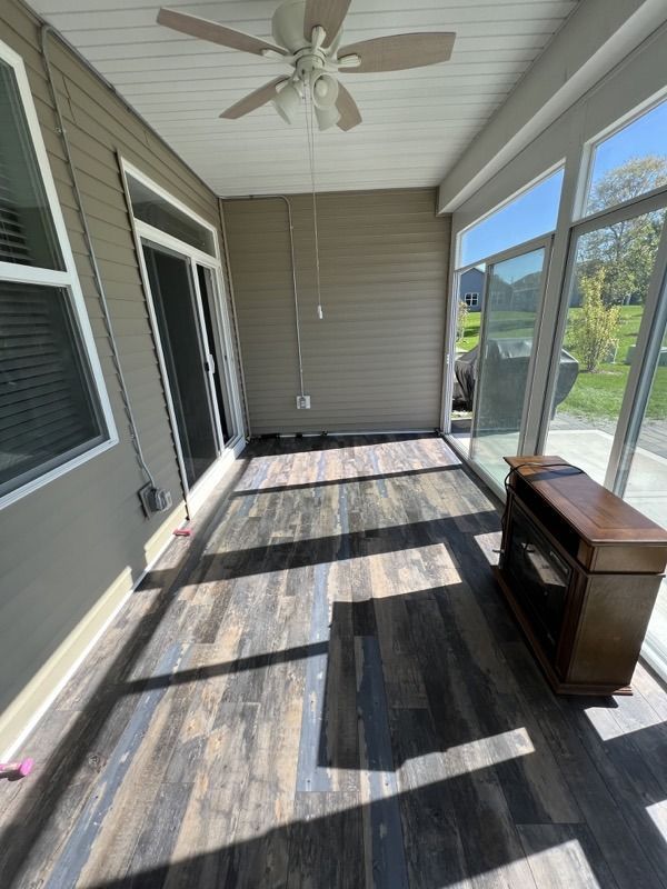 Covered porch with gray siding, dark wood deck, ceiling fan, and a small chest near the wall.