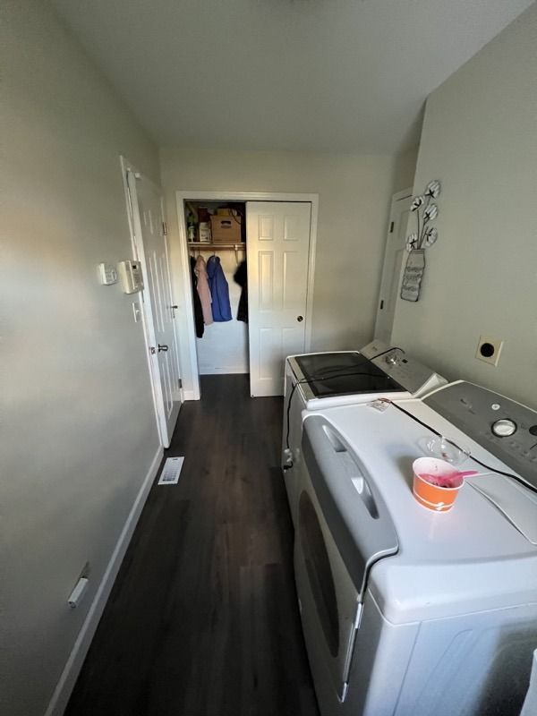 Narrow laundry room with white walls, dark floor, washer and dryer, and a closet at the far end.