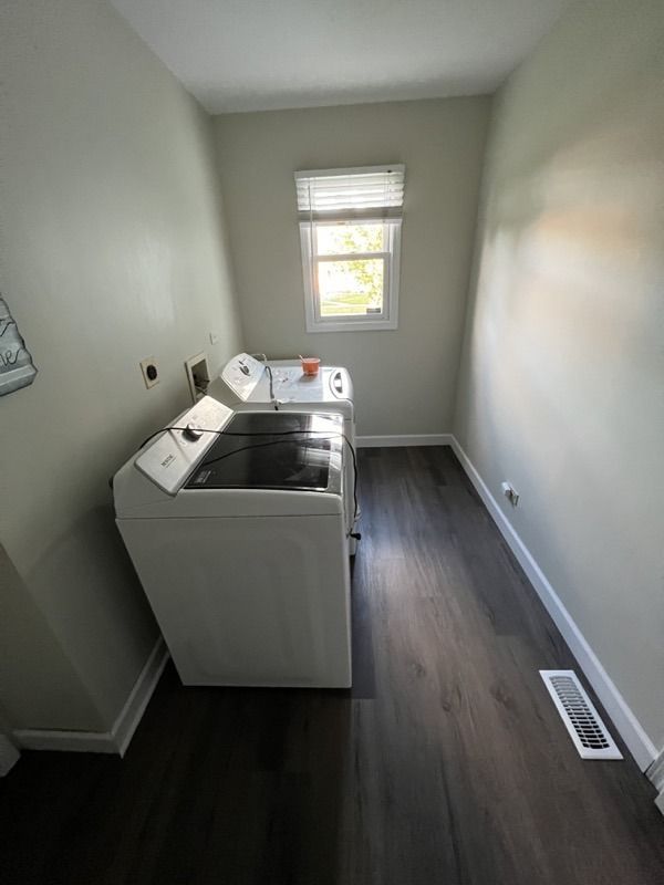 Laundry room with washer and dryer, gray walls, window, and dark wood floor.