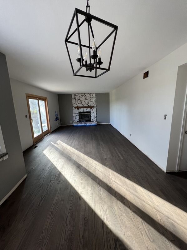 Empty modern dining room with dark floors, geometric black chandelier, and sunlight streaming in from the left.