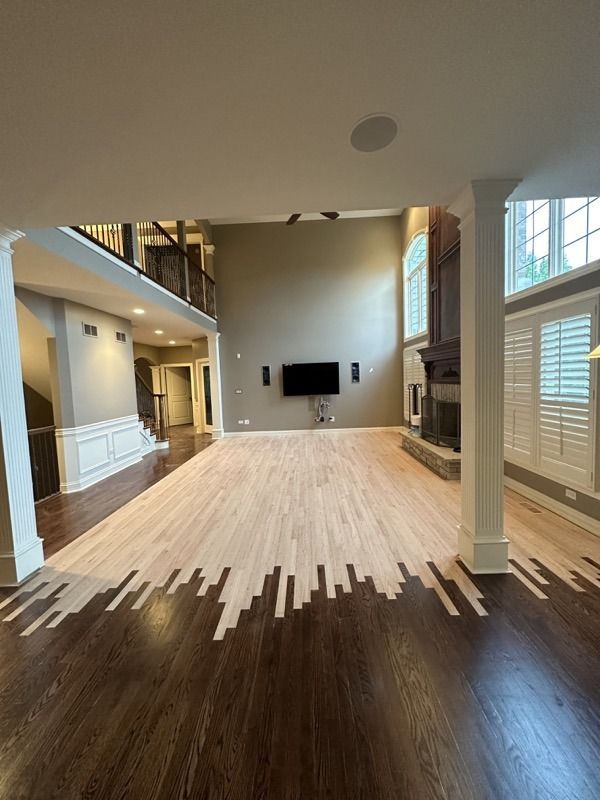 Empty living room with dark hardwood, white walls, high ceiling, and large windows.