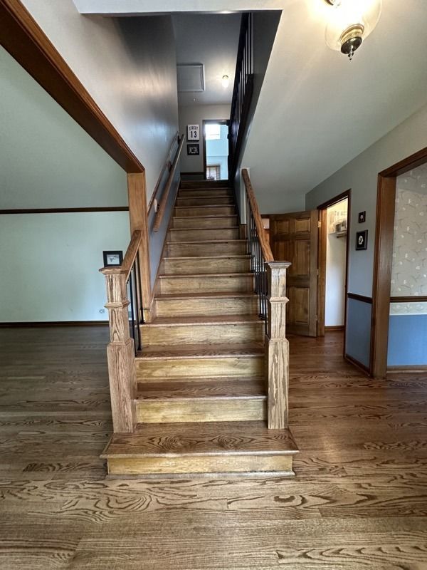 Wooden staircase in a hallway with hardwood floors and white walls, leading to an upper landing.