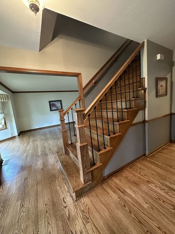 Wooden staircase with railing in a bright home hallway with hardwood floors