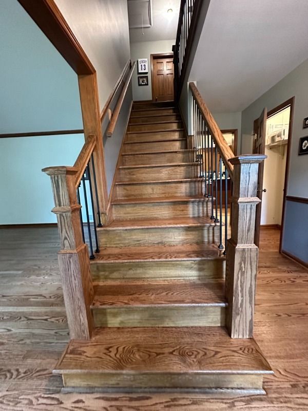 Wooden staircase in a house with railings and hallway landing at the top.