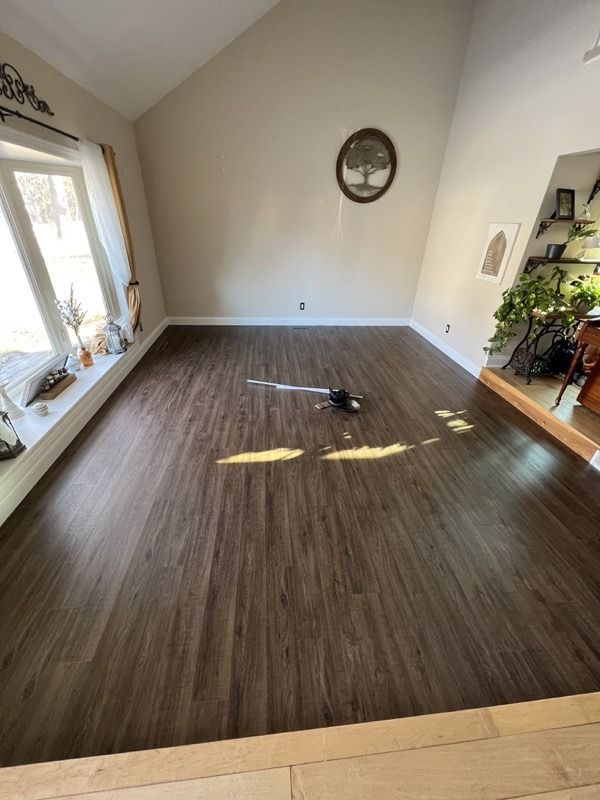 Empty living room with dark wood floor, white walls, large window, and a wall mirror.