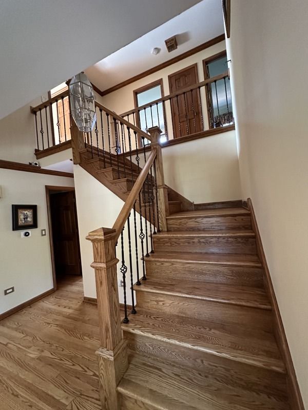 Wooden staircase with banister in a bright home interior, leading to an upper landing.