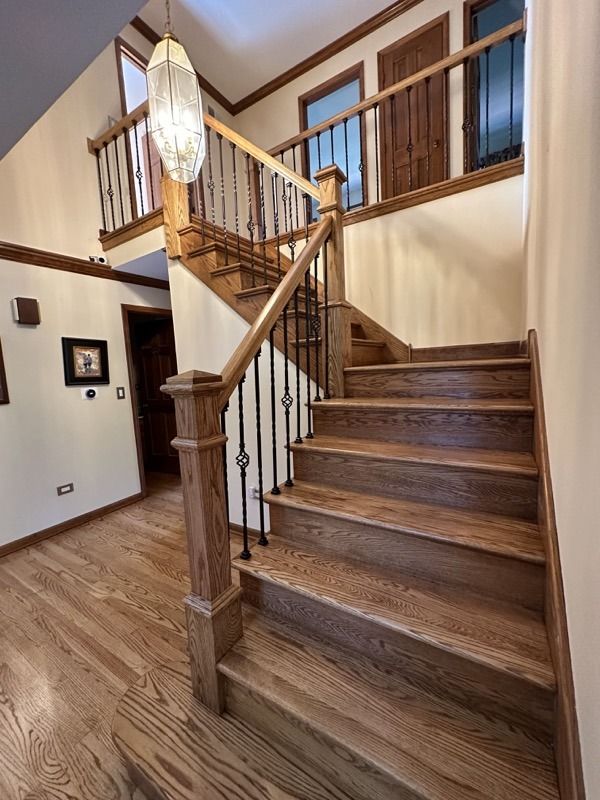 Wooden staircase with railing in a home entryway, featuring a hanging chandelier and tiled floor.