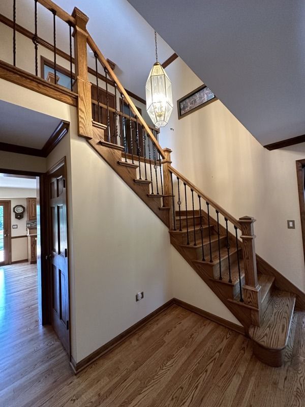 Wooden staircase with railing in a home entryway, beside a hallway and hanging light fixture