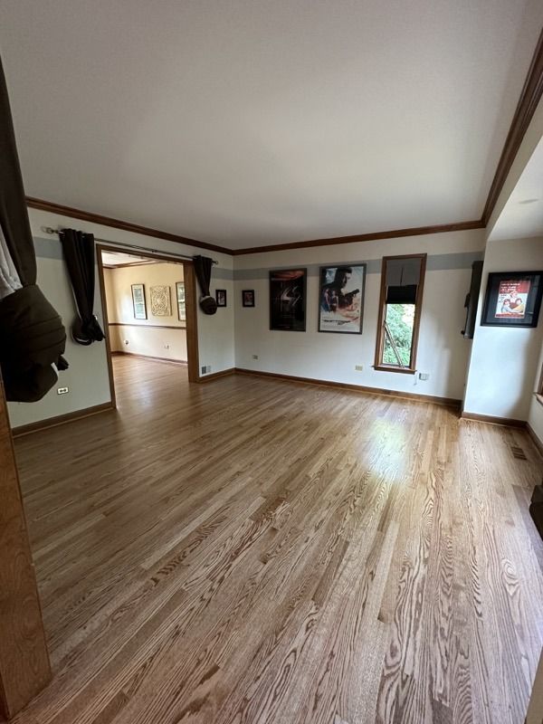 Empty living room with light wood floors, white walls, dark trim, and framed art on the far wall.