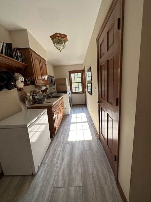 Narrow kitchen with wooden cabinets, white appliances, and sunlight streaming through a back window.