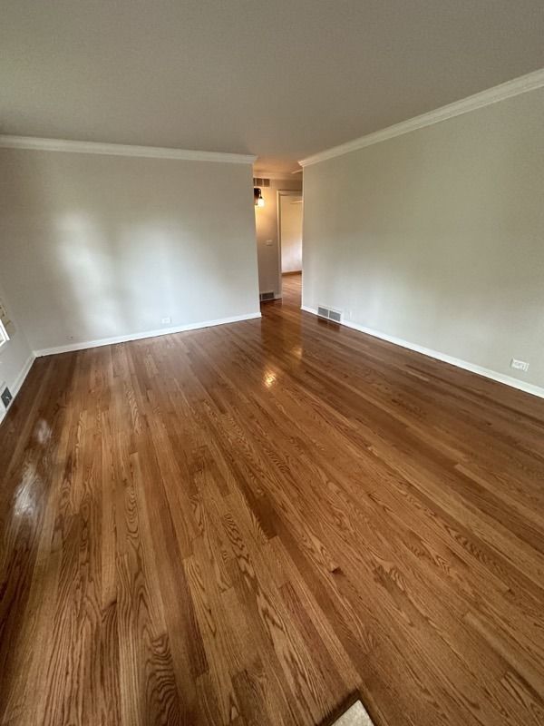 Empty room with glossy hardwood floors, beige walls, and a doorway leading to a hallway.