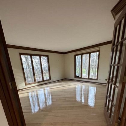 Empty sunlit living room with polished wood floors and large windows overlooking trees
