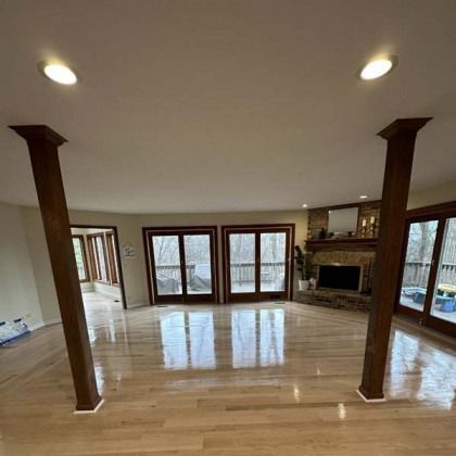 Spacious empty living room with hardwood floors, wood columns, a fireplace, and large windows.
