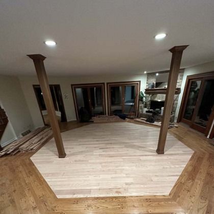 Empty unfinished room with light wood floors, exposed posts, and large windows and doors.