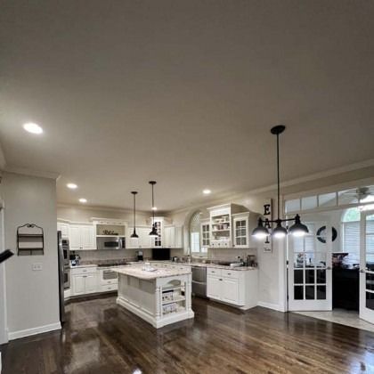 Bright modern kitchen with white cabinets, island, pendant lights, and dark hardwood floors
