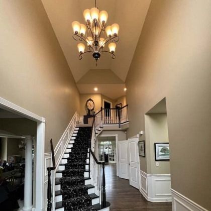 Elegant entry hallway with a black staircase, chandelier, and beige walls in a spacious home.