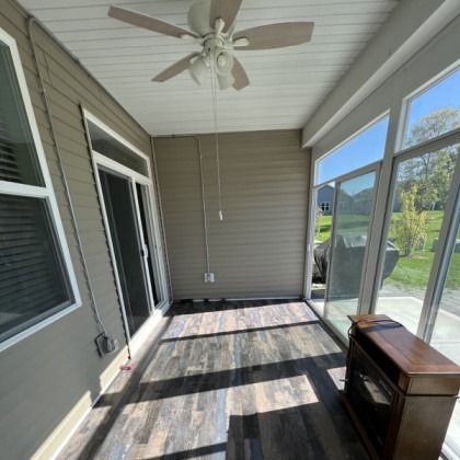 Enclosed sunroom with ceiling fan, gray walls, wood-look floor, and large windows overlooking a yard