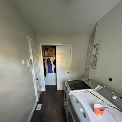 Laundry room with white washer and dryer, a hanging jacket, and an open closet in the back.