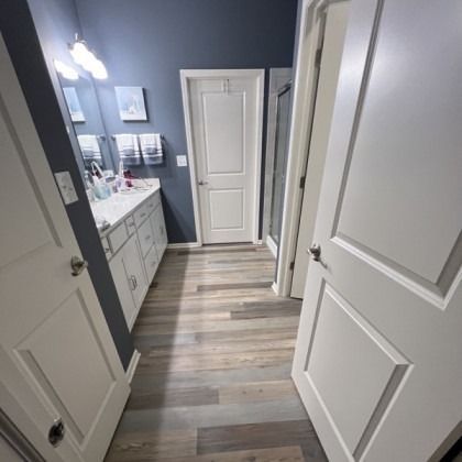 Narrow bathroom hallway with white doors, gray walls, and wood-look flooring.