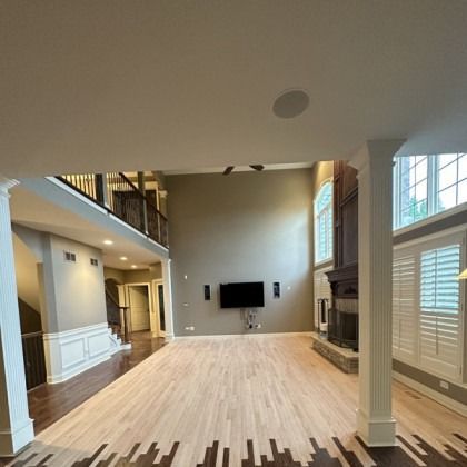 Empty living room with hardwood floors, high ceilings, staircase, fireplace, and wall-mounted TV.
