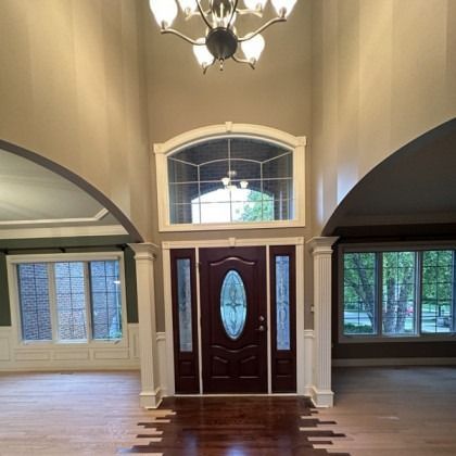Grand foyer with dark wood front door, arched windows, chandelier, and hardwood floors.