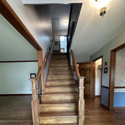 Wooden staircase in a home entryway with light walls, wood trim, and hallways on both sides.