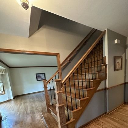 Interior view of a home with a wooden staircase, banister, and hardwood floors leading to an open room