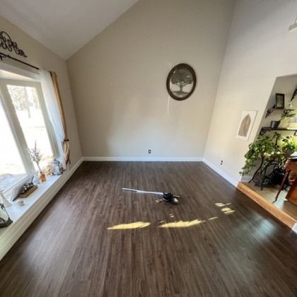 Empty living room with wood-look flooring, beige walls, and sunlight streaming through a window.